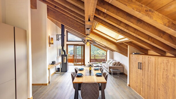 Un vaste espace dédié à la salle à manger, avec une table et des chaises en bois, un canapé et une vue sur l’extérieur grâce à de grandes fenêtres.