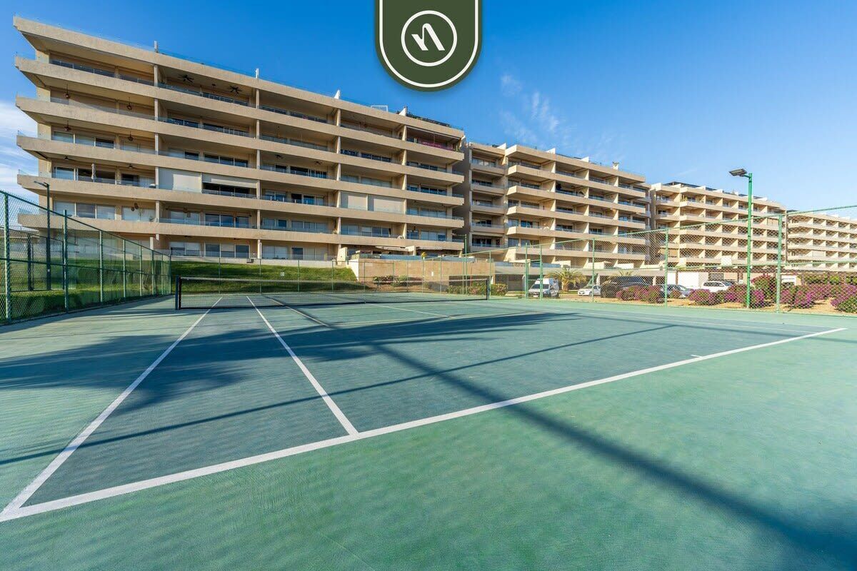 A multi-story building with a tennis court in front.