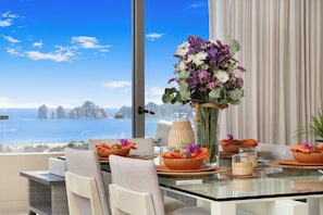 A dining area with a glass table, chairs, and a view of the sea.