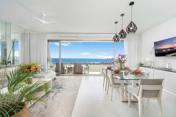 A modern living room with a dining area, large windows, and a view of the ocean.