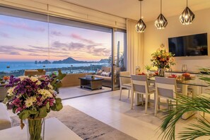 A modern living room with a large glass door leading to a balcony overlooking a scenic view of the sea and mountains.