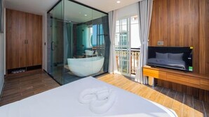 A modern hotel room with a glass-enclosed shower, a large bed, a TV, and a balcony with a view. - Merci Sunset Town Phu Quoc (Phu Quoc Island)