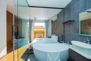 A modern hotel room with a glass shower enclosure, a large bathtub, and a separate sink.