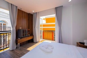 A hotel room with a bed, a bench with a TV, and a balcony with a railing. - Merci Sunset Town Phu Quoc (Phu Quoc Island)