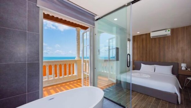 A modern hotel room with a balcony, a large bathtub, and a bed with a wooden headboard. - Merci Sunset Town Phu Quoc (Phu Quoc Island)