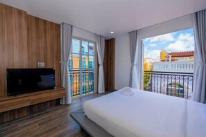 A hotel room with a bed, a flat-screen TV, a balcony with a railing, and a view of buildings. - Merci Sunset Town Phu Quoc (Phu Quoc Island)