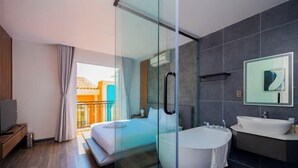 A modern hotel room with a glass-enclosed shower, a large bathtub, a bed, a TV, and a balcony with a view. - Merci Sunset Town Phu Quoc (Phu Quoc Island)