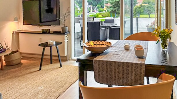 A modern dining area with a table set for two, a bowl, and a vase with flowers.