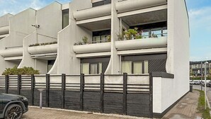 A modern multi-story building with balconies, a gated entrance, and a parking area.