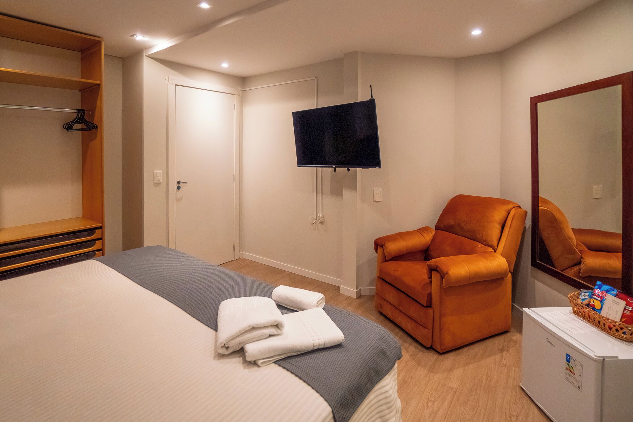 Een hotelkamer met een bed, een televisie, een stoel, een spiegel en een minibar.