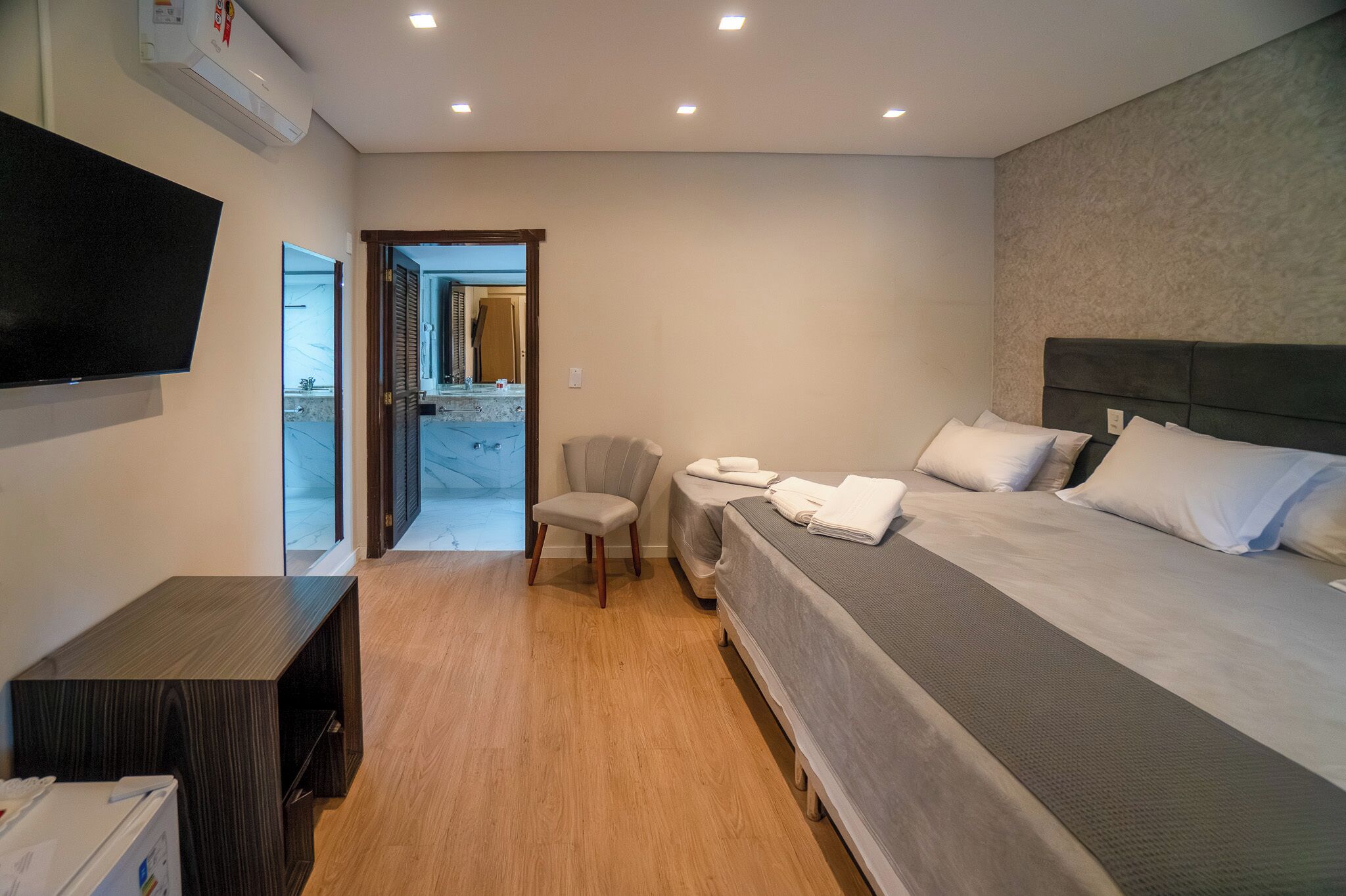 A hotel room with a bed, a TV, a chair, and a desk.
