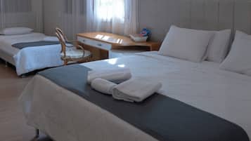 A hotel room with two beds, a desk, a chair, and a window with sheer curtains.