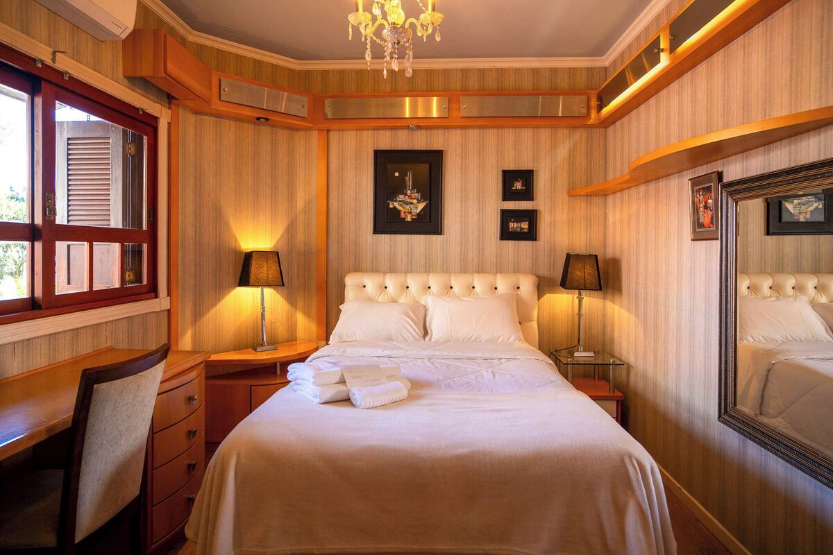 Une chambre d’hôtel avec un grand lit, deux tables de chevet, une chaise, un bureau et un grand miroir.