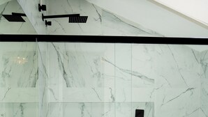 Ein modernes Badezimmer mit Marmorwänden, einer Duschkabine aus Glas und einem horizontalen schwarzen Akzent.
