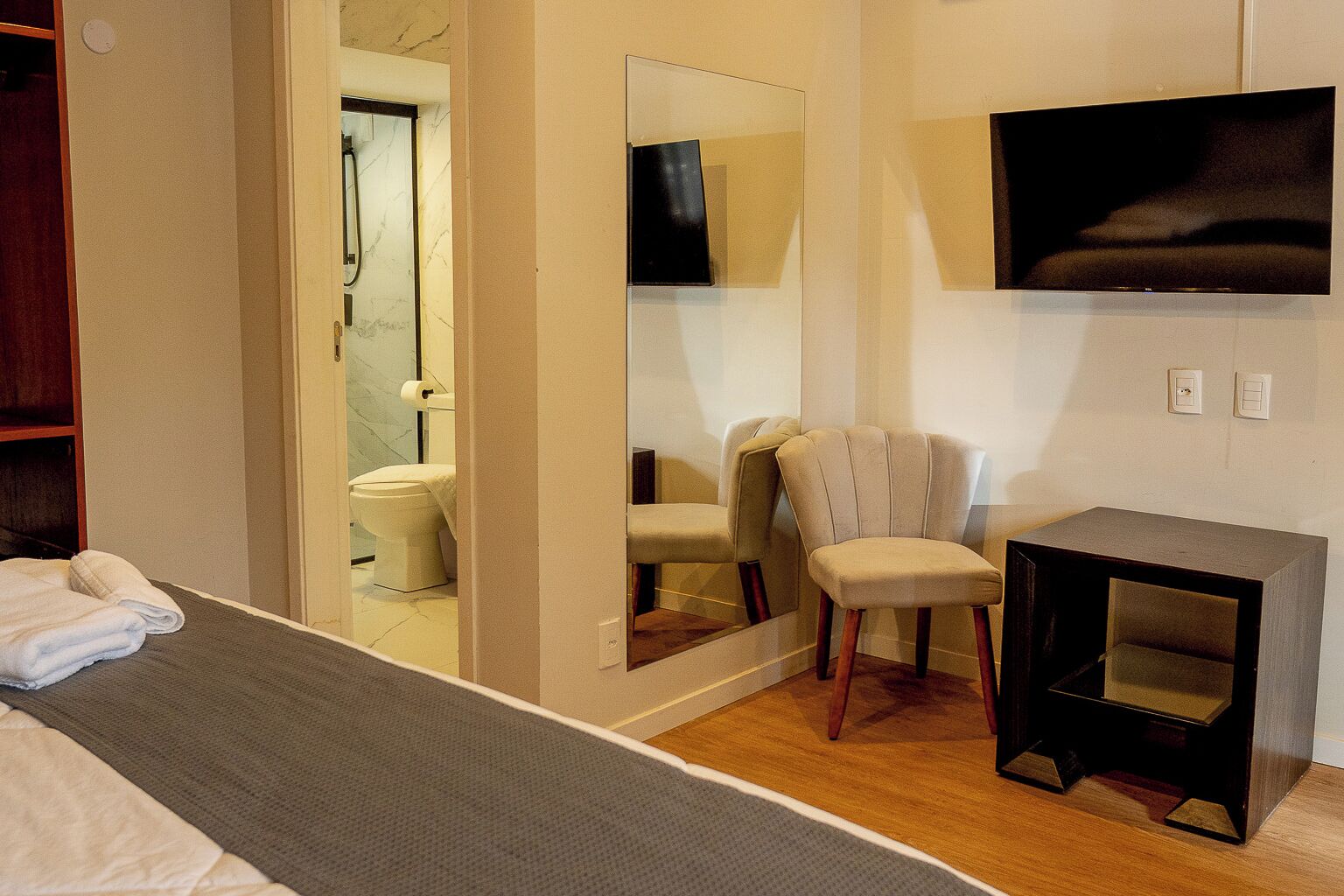 A hotel room with a bed, a chair, a small table, a television, and a mirror.