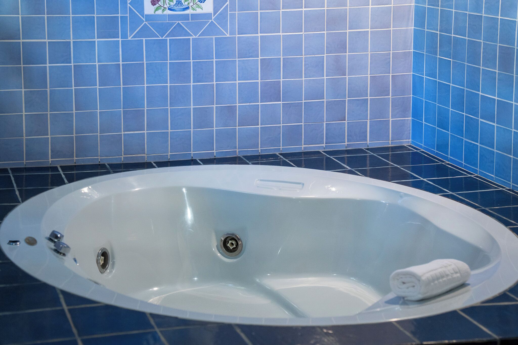 Una bañera blanca con desagüe, una toalla y un estante pequeño en un cuarto con paredes de azulejos azules.