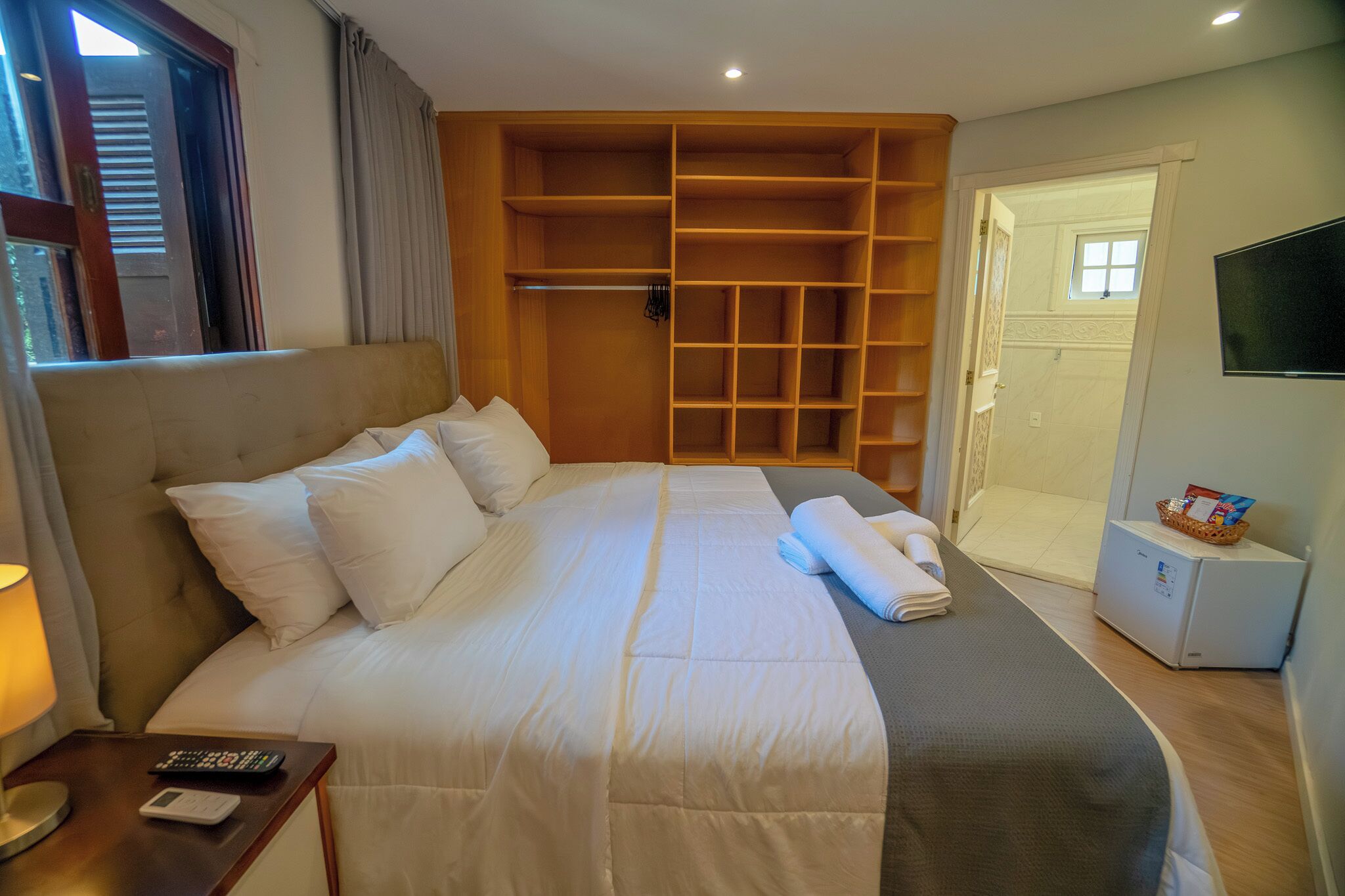 A hotel room with a large bed, a wardrobe, a TV, and a small table with a remote control.