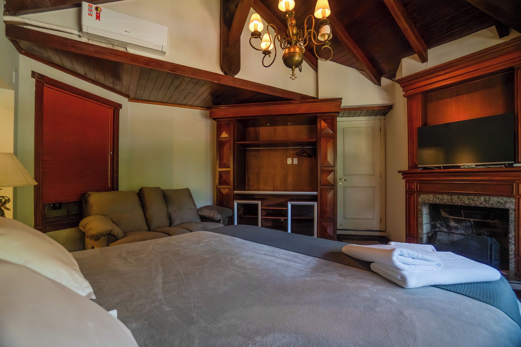 A hotel room with a bed, a seating area, a TV, a fireplace, and a wardrobe.