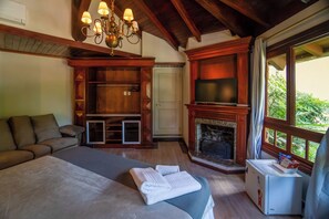 Un dormitorio con cama, televisor, chimenea y ventana con vistas a follaje.
