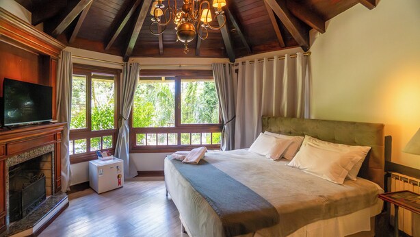 Ein Schlafzimmer mit einem Bett, einem Fernseher, einem Kamin und einem Fenster mit Vorhängen.