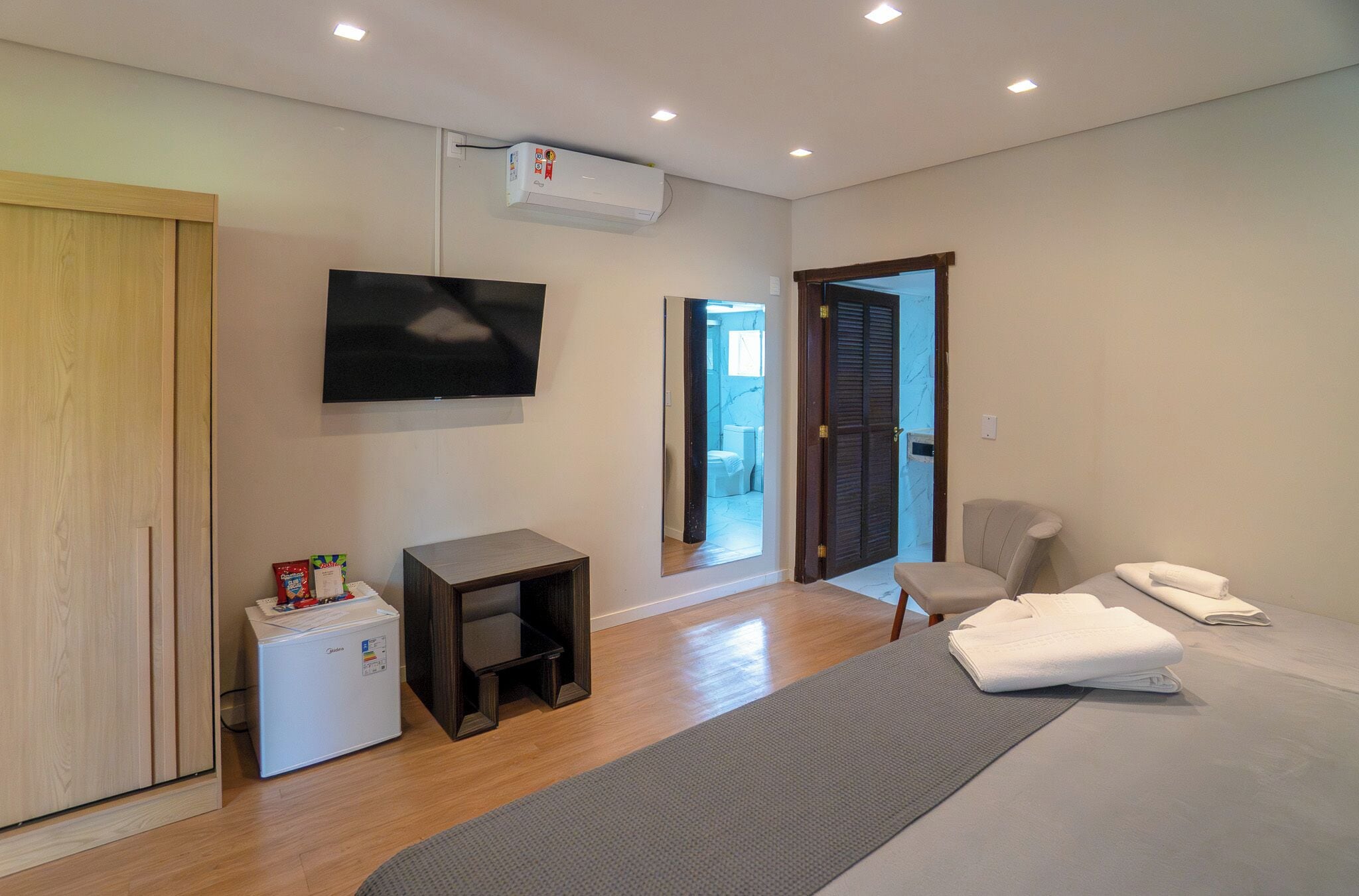 Ein modernes Schlafzimmer mit Bett, Fernseher, kleinem Kühlschrank, Schreibtisch und Stuhl.