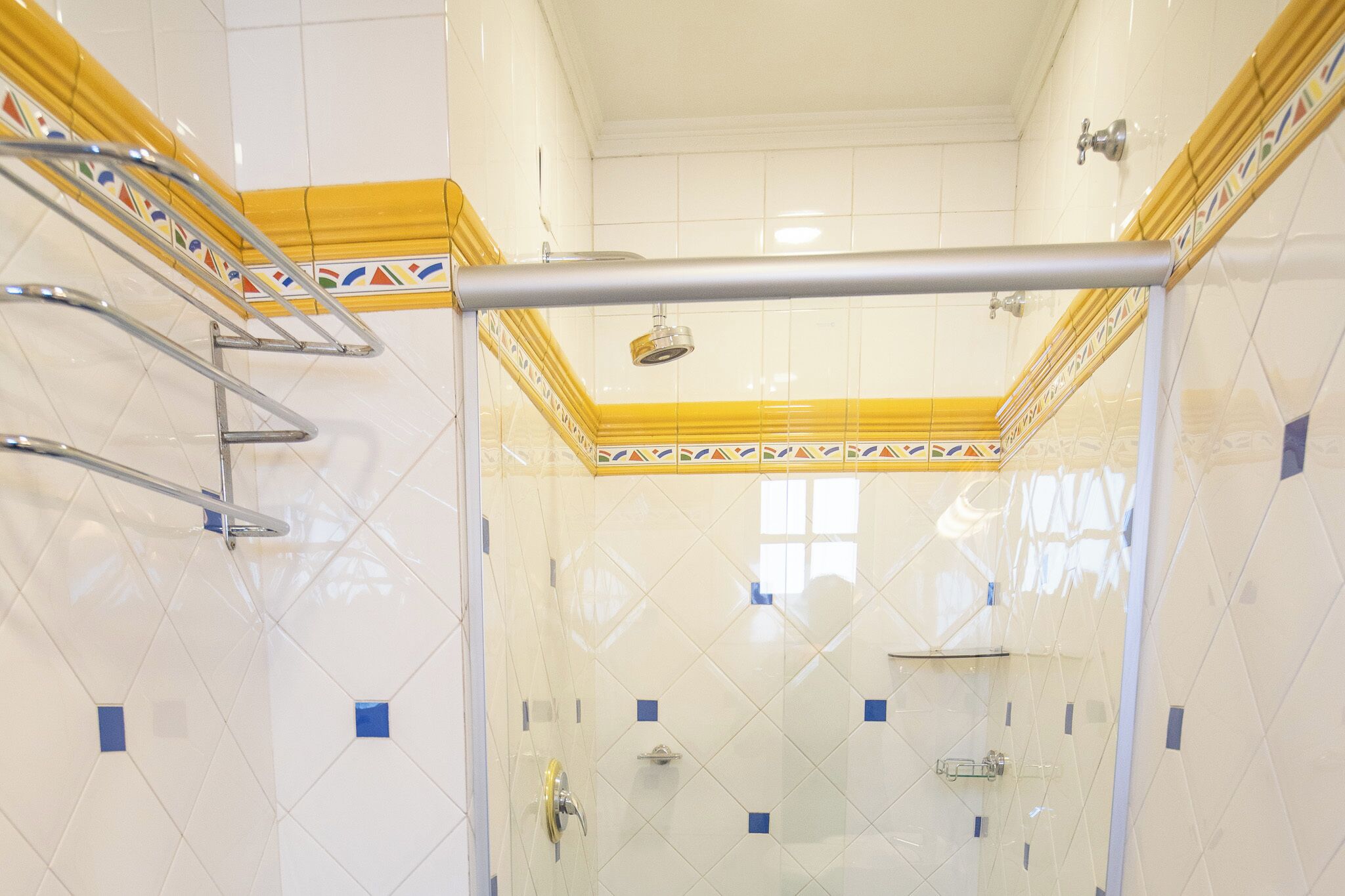 A bathroom with white tiled walls, a yellow decorative border, and a glass shower enclosure.
