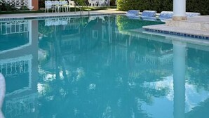 Una piscina cristalina con borde de azulejos y algunas sillas de descanso alrededor.