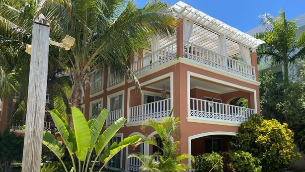 Un edificio de dos pisos con balcón, rodeado de plantas tropicales y un césped bien cuidado.