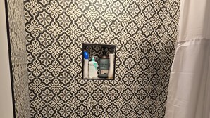 Ein Badezimmer mit gemusterten Fliesen, einer Duschvorhangs und einem Ablagefach mit Pflegeprodukten.