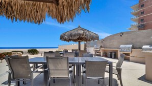 An outdoor patio with a table and chairs, a grill, and a view of the ocean. - Viva Condominiums Viva 28 (San José del Cabo)