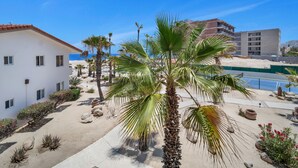 A white building with multiple windows, a palm tree, and a sandy courtyard. - Viva Condominiums Viva 28 (San José del Cabo)
