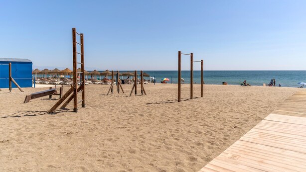 A beach with wooden structures, a blue building, and beach umbrellas. - Cozy apartment in Fuengirola (Fuengirola)