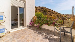 Un balcon donnant sur une colline, une chaise et un bâtiment dont le volet est fermé.