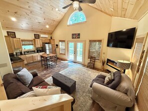 A spacious living area with a high ceiling, wooden beams, a fireplace, and a large TV.