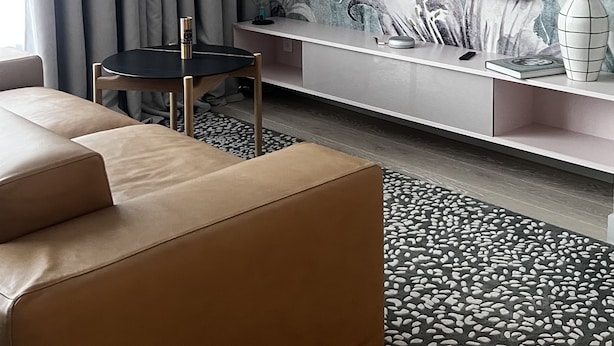 A modern living room with a flat-screen TV, a sofa, a small table, and a decorative wall with a plant mural.