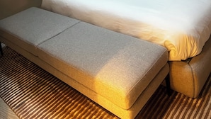 A neatly made bed with a white duvet and a black pillow, a grey bench, and a wall with a leaf pattern.