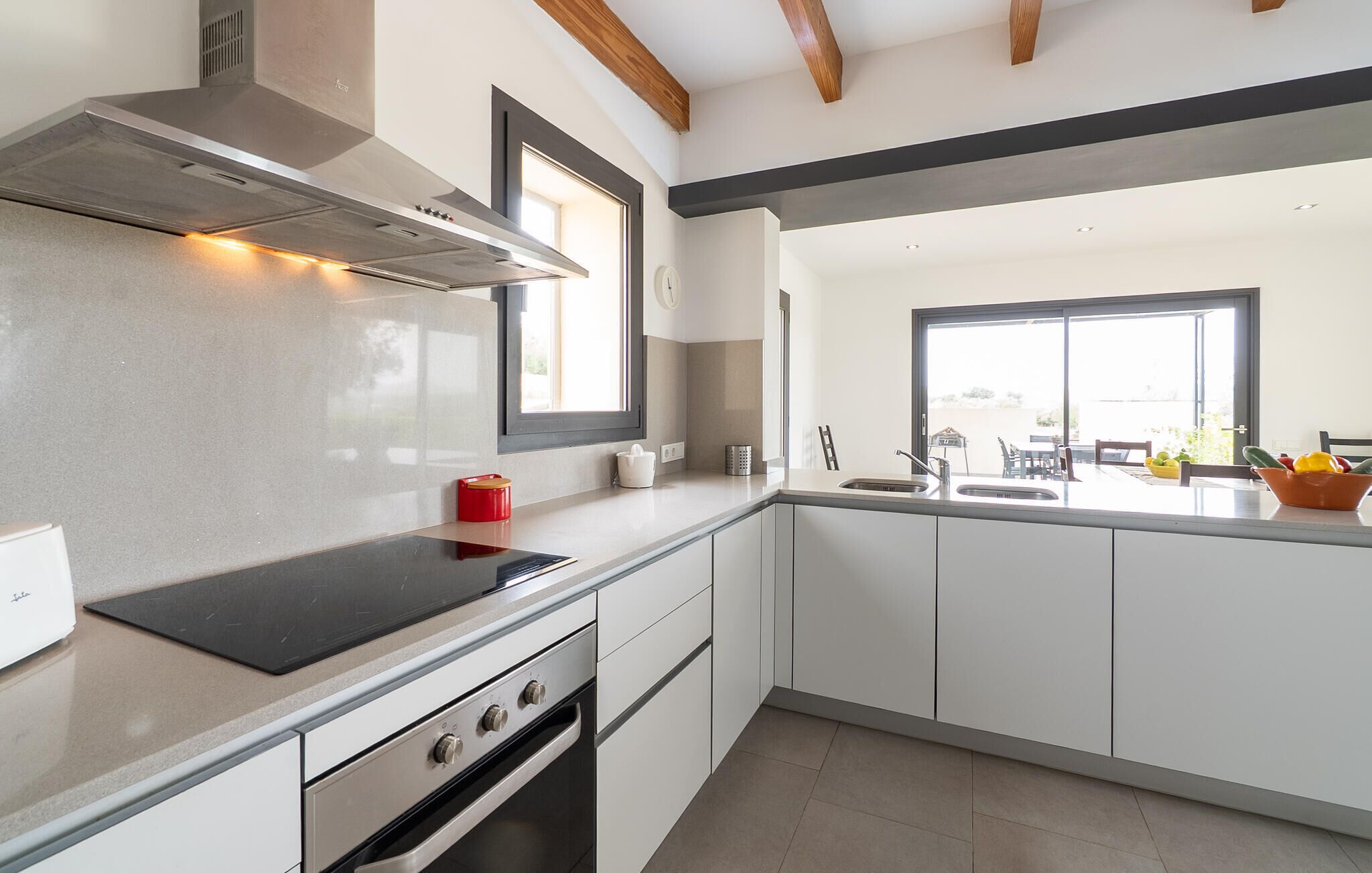 Een moderne keuken met witte kasten, een roestvrijstalen afzuigkap en een groot raam dat zorgt voor veel daglicht.
