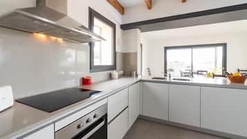 A modern kitchen with white cabinetry, a stainless steel range hood, and a large window providing natural light.