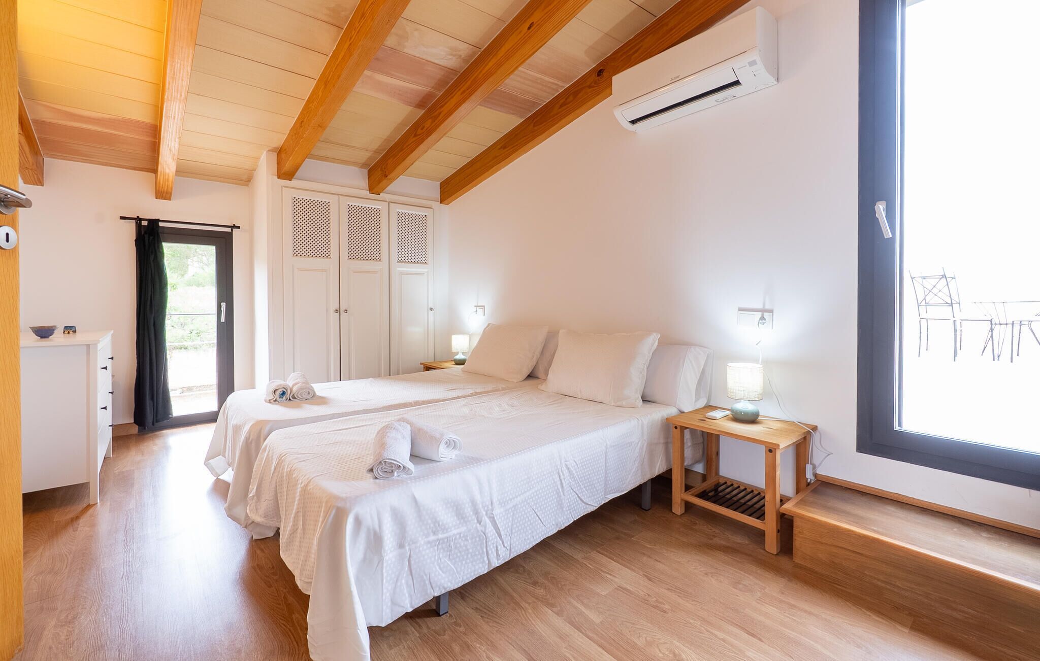 Ein Schlafzimmer mit zwei Betten, Holzboden, Kleiderschrank, Klimaanlage und einem Fenster mit Aussicht.