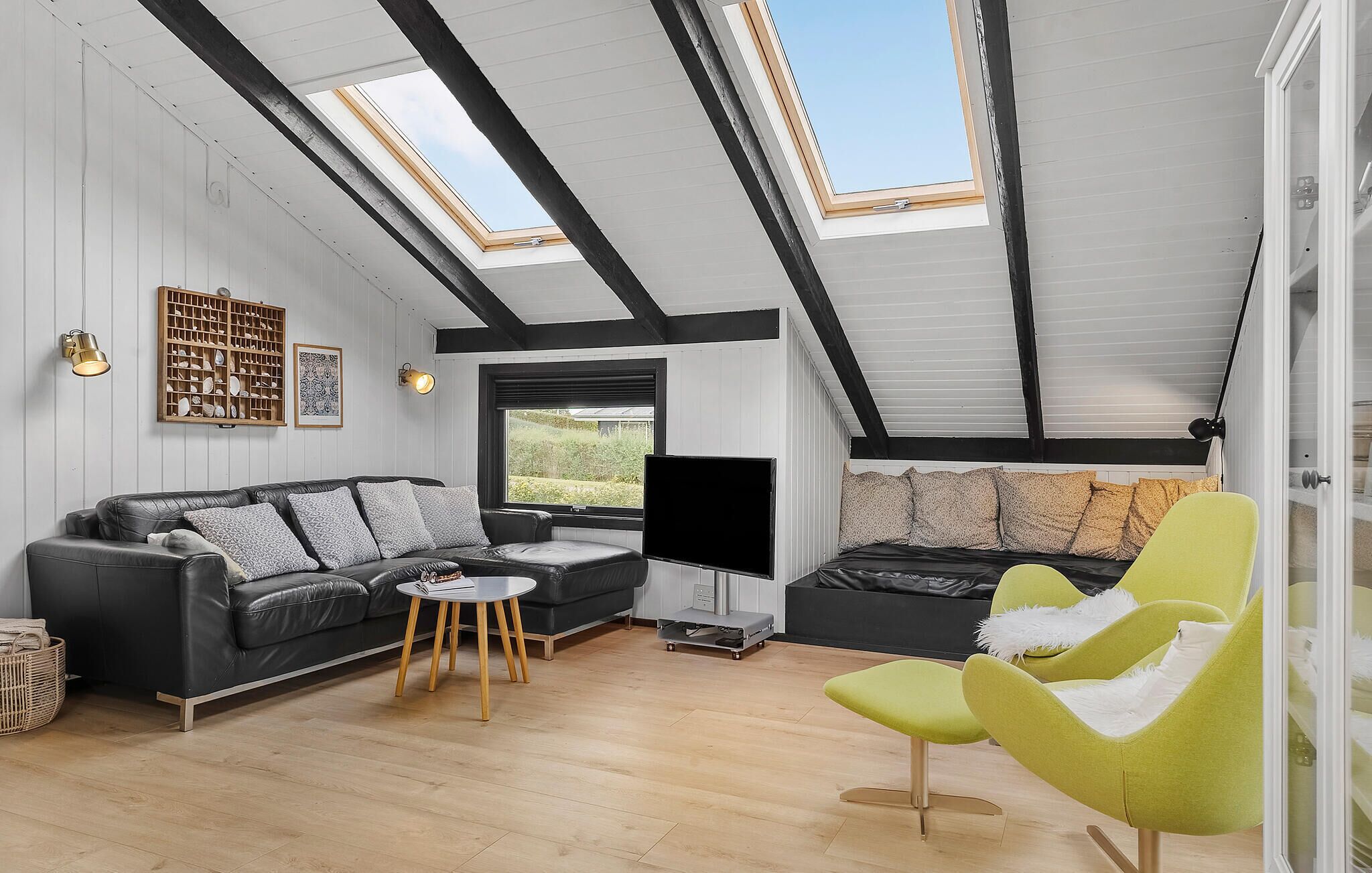 A modern loft with a high ceiling, skylights, a black leather sofa, a green armchair, and a wooden coffee table.