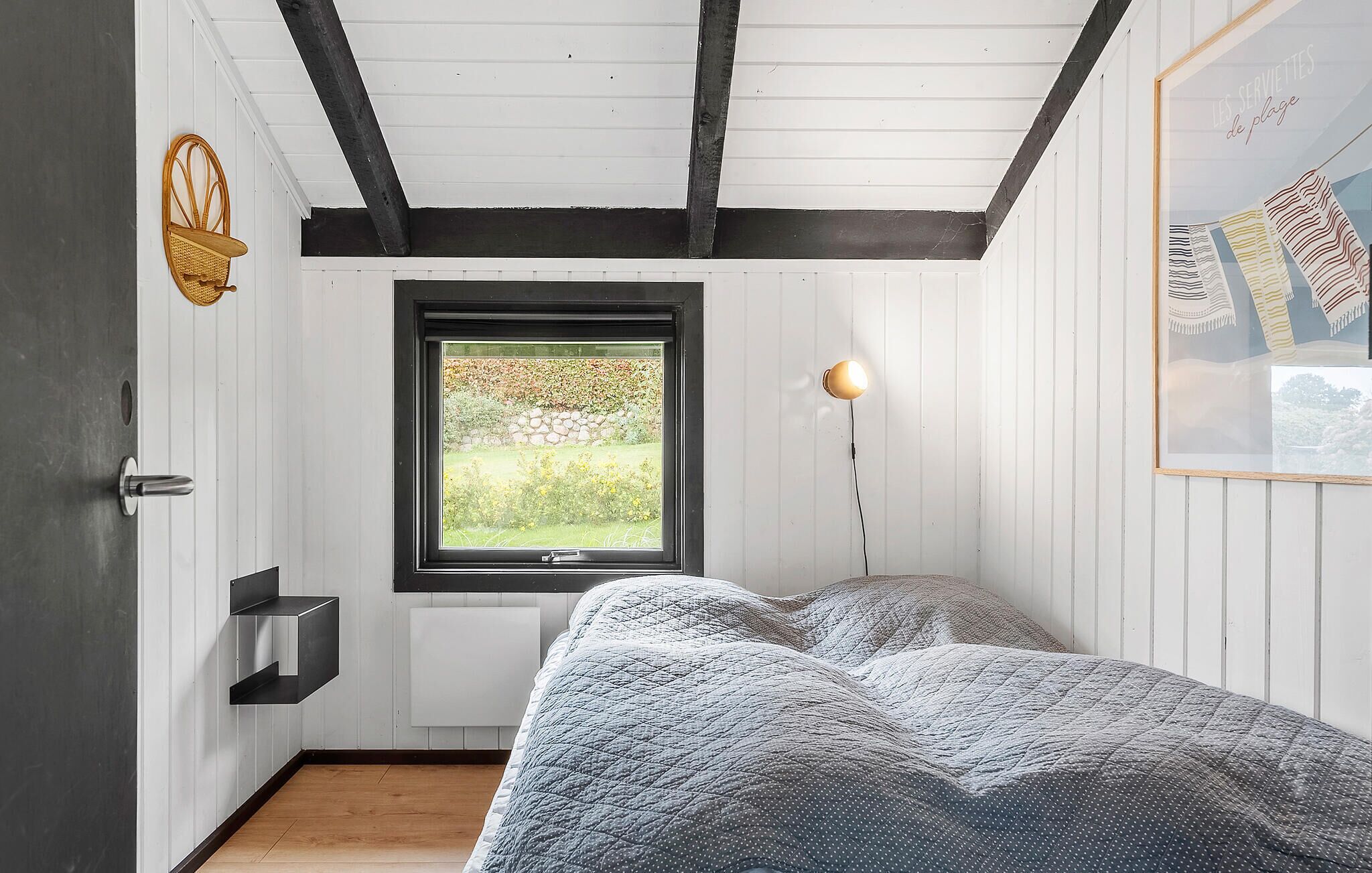 A bedroom with a bed, a window, a wall-mounted shelf, and a wall-mounted light fixture.