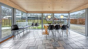 A covered patio with a table and chairs, large windows, and a view of the backyard.