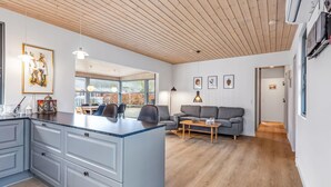 A modern living room with a grey sofa, a wooden coffee table, and a kitchen area with grey cabinets and a blue countertop.