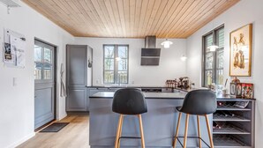 A modern kitchen with a central island, two bar stools, a wine rack, and a large window.