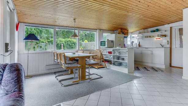 A modern kitchen with white cabinets, a dining area with a wooden table and chairs, and large windows offering a view of greenery outside. - Lovely home in Haderslev with WiFi (Haderslev)