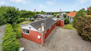 A red building with a gravel driveway, surrounded by greenery and other houses. - Lovely home in Haderslev with WiFi (Haderslev)
