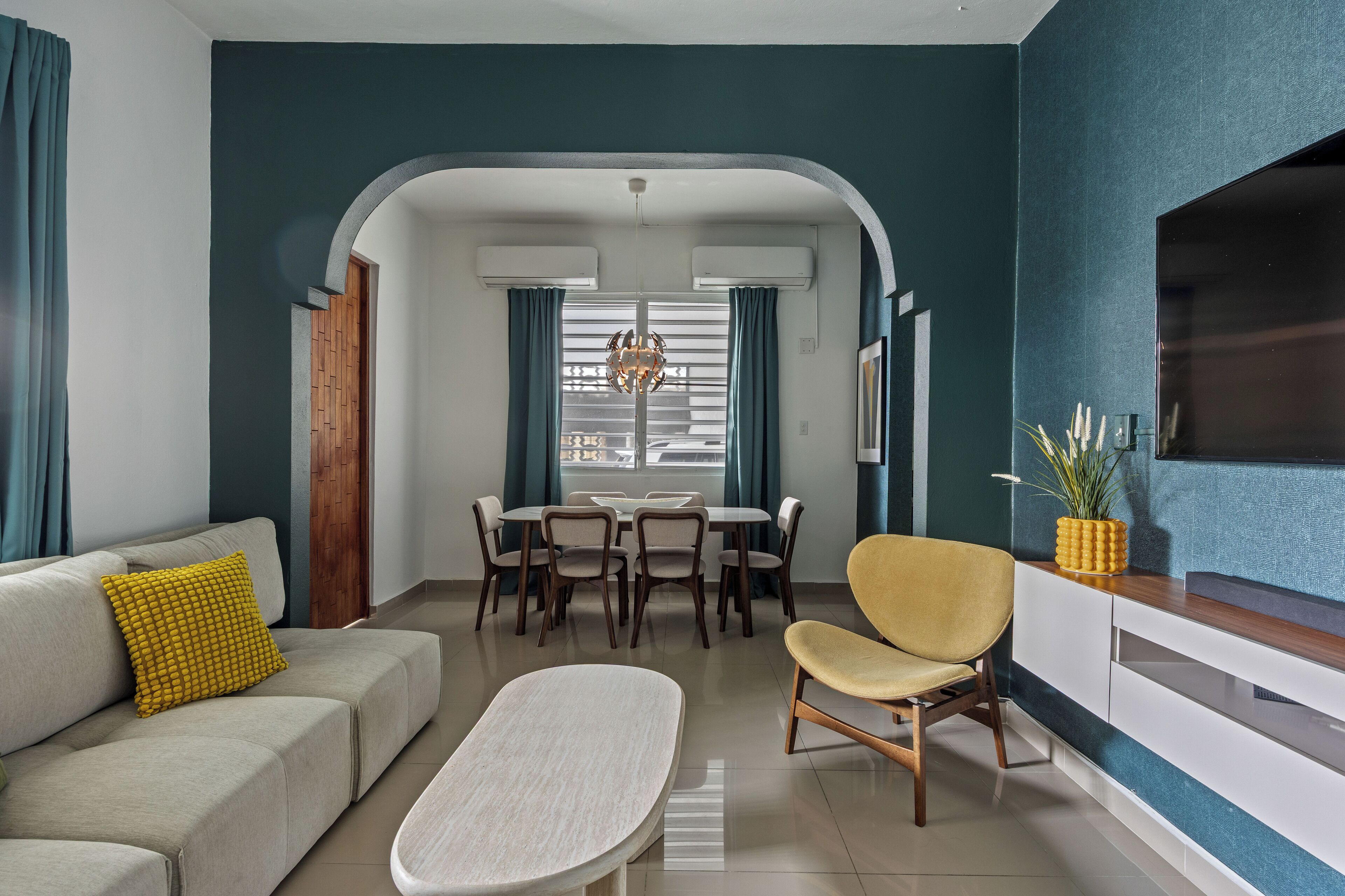 Ein modernes Wohnzimmer mit Sofa, Couchtisch, Esstisch mit Stühlen und einem an der Wand befestigten Fernseher.