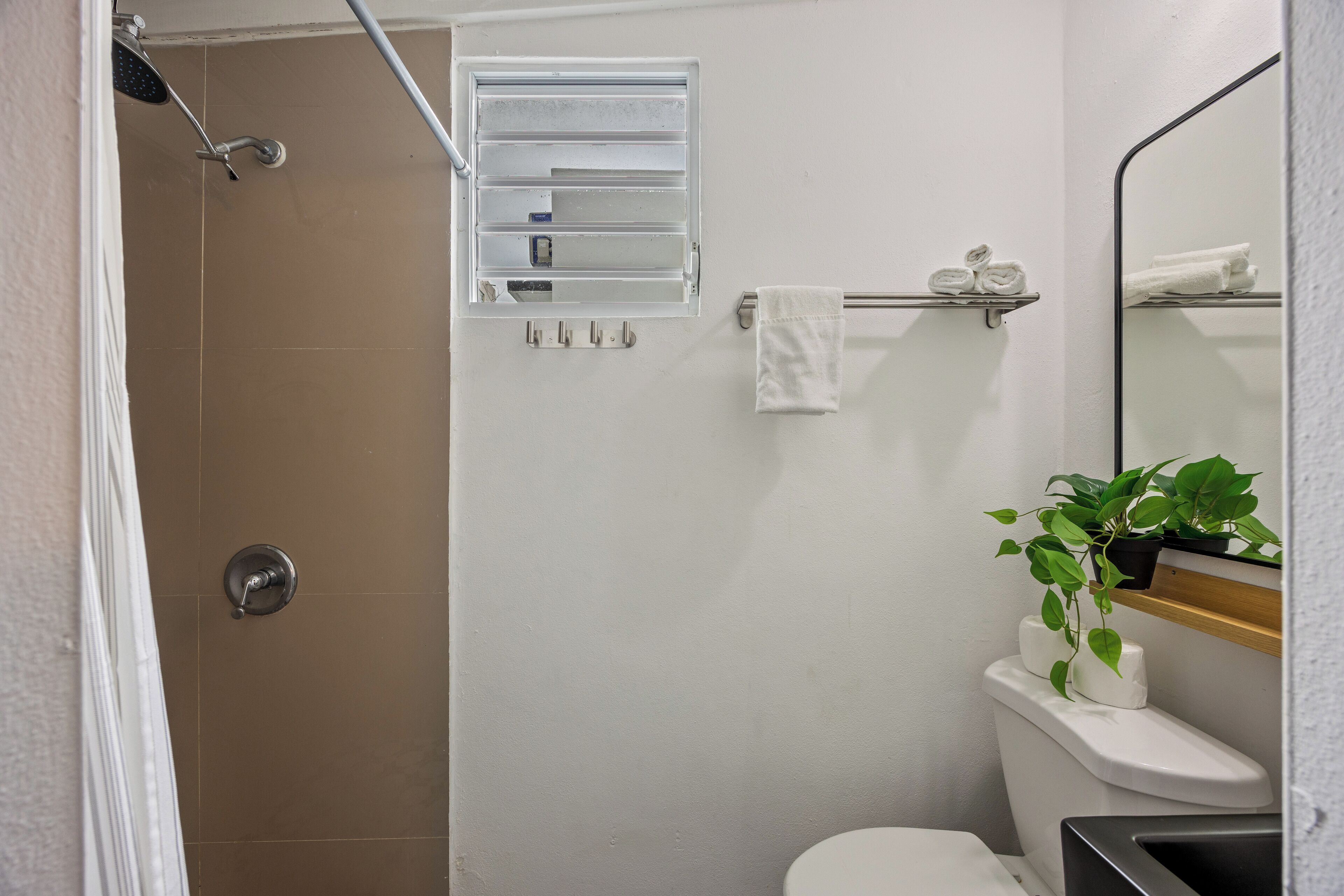 Une salle de bain avec une douche, des toilettes et un lavabo. On y trouve un porte-serviettes avec des serviettes et une petite étagère avec des articles de toilette.