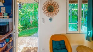 Una habitación con una silla amarilla, un tapiz decorativo y vistas a un jardín exuberante por una ventana.