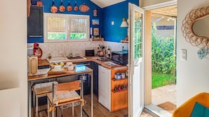 Cocina compacta con refrigerador, microondas y un lavamanos pequeño. Hay dos taburetes de bar y una ventana con persianas.
